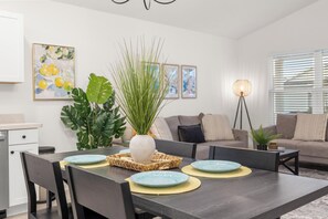 A modern living room with a dining table set for four, a sofa, a floor lamp, and a large plant. - 2BR · 2 Bath · Golf Cart · Mins to Eastport Sq (Sumterville)