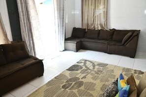 A living room with a sectional sofa, a patterned rug, and a view of the outside through a window with curtains. - Pousada Bem-Te-Vi (Aracaju)