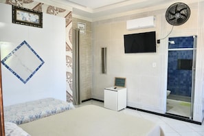 A hotel room with a bed, a small bedside table, a TV mounted on the wall, a shower area, and a fan. - Pousada Bem-Te-Vi (Aracaju)