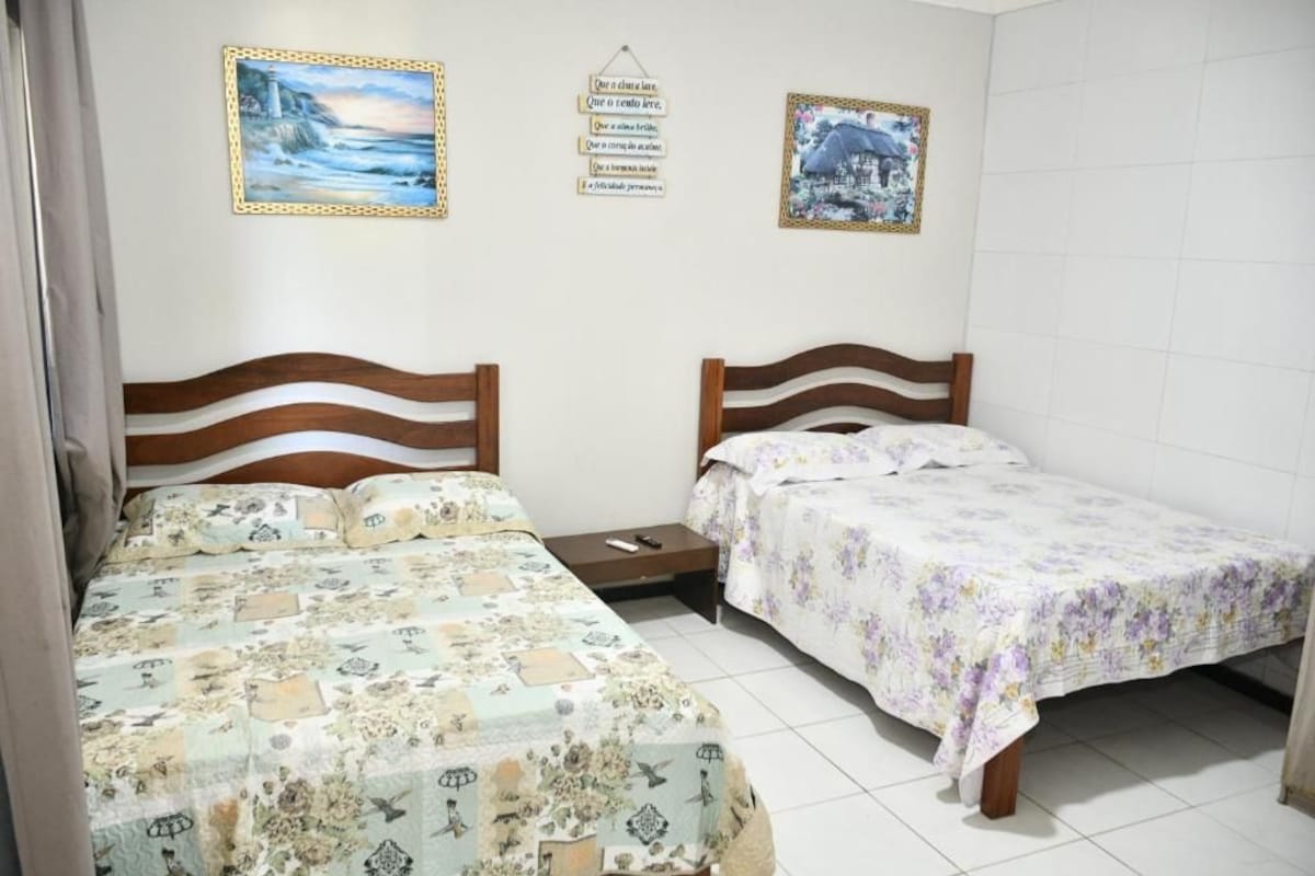 A bedroom with two beds, a nightstand, and a wall with framed pictures.