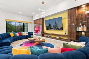 Un salon moderne avec un grand canapé d’angle, une table basse ronde et un téléviseur à écran plat fixé sur un mur jaune.