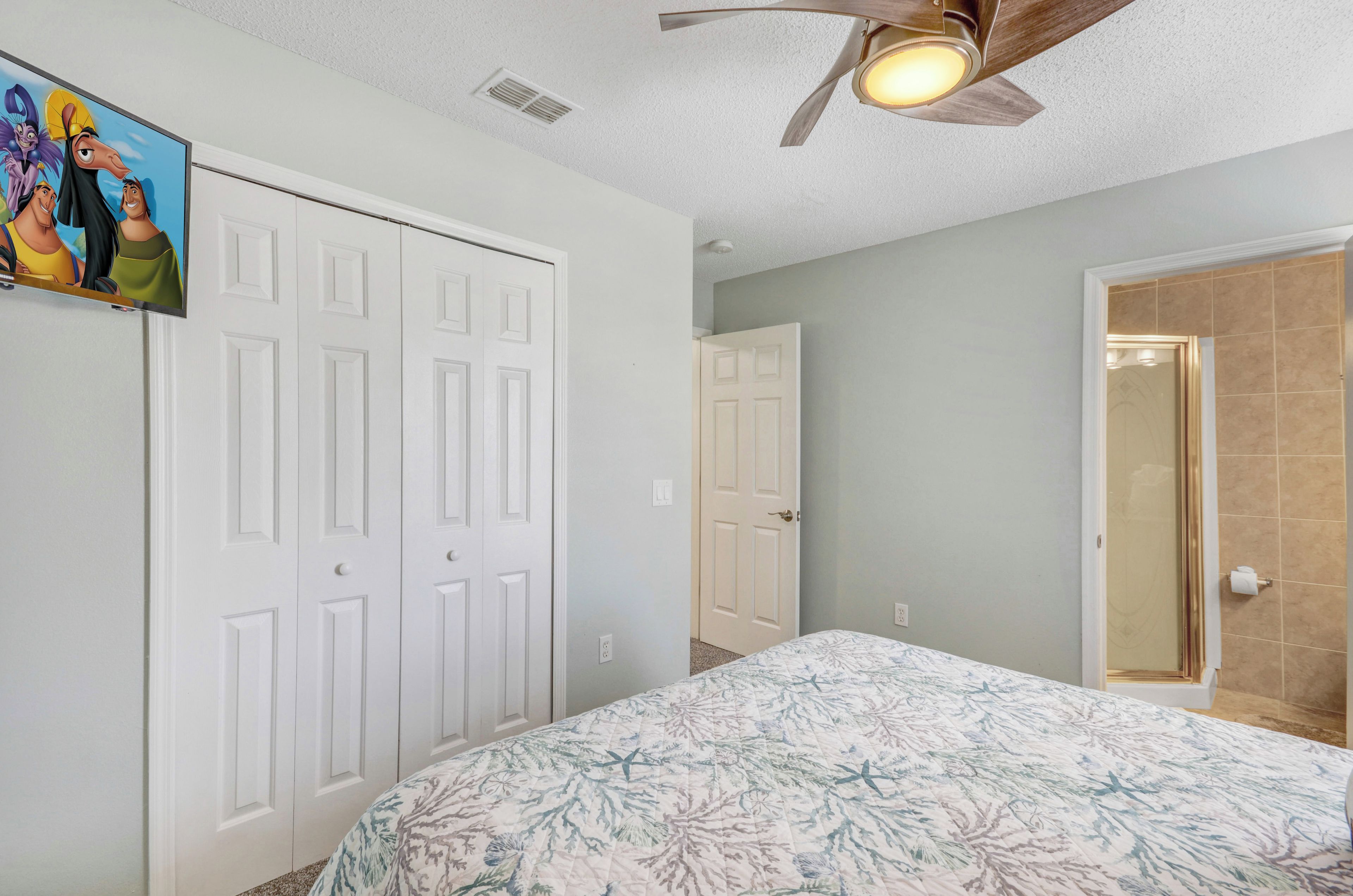 A bedroom with a bed, a ceiling fan, and a door.