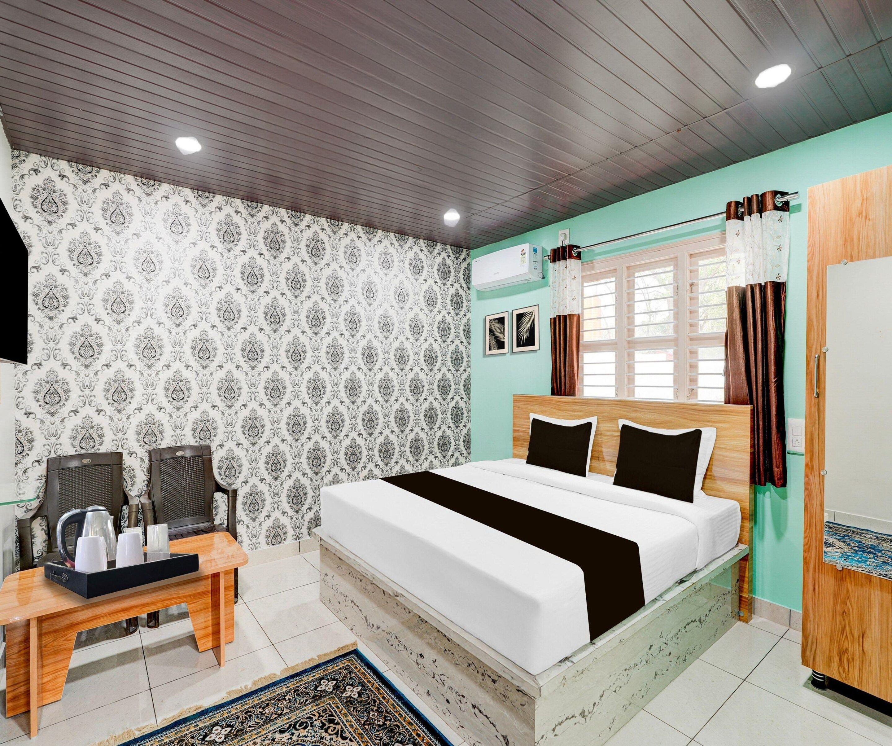 A bedroom with a bed, a desk, chairs, a window with curtains, and a wall air conditioner.