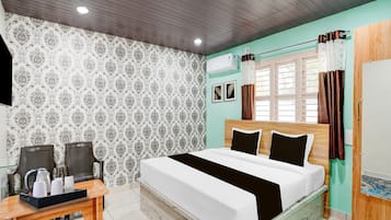 A bedroom with a bed, a desk, chairs, a window with curtains, and a wall air conditioner.