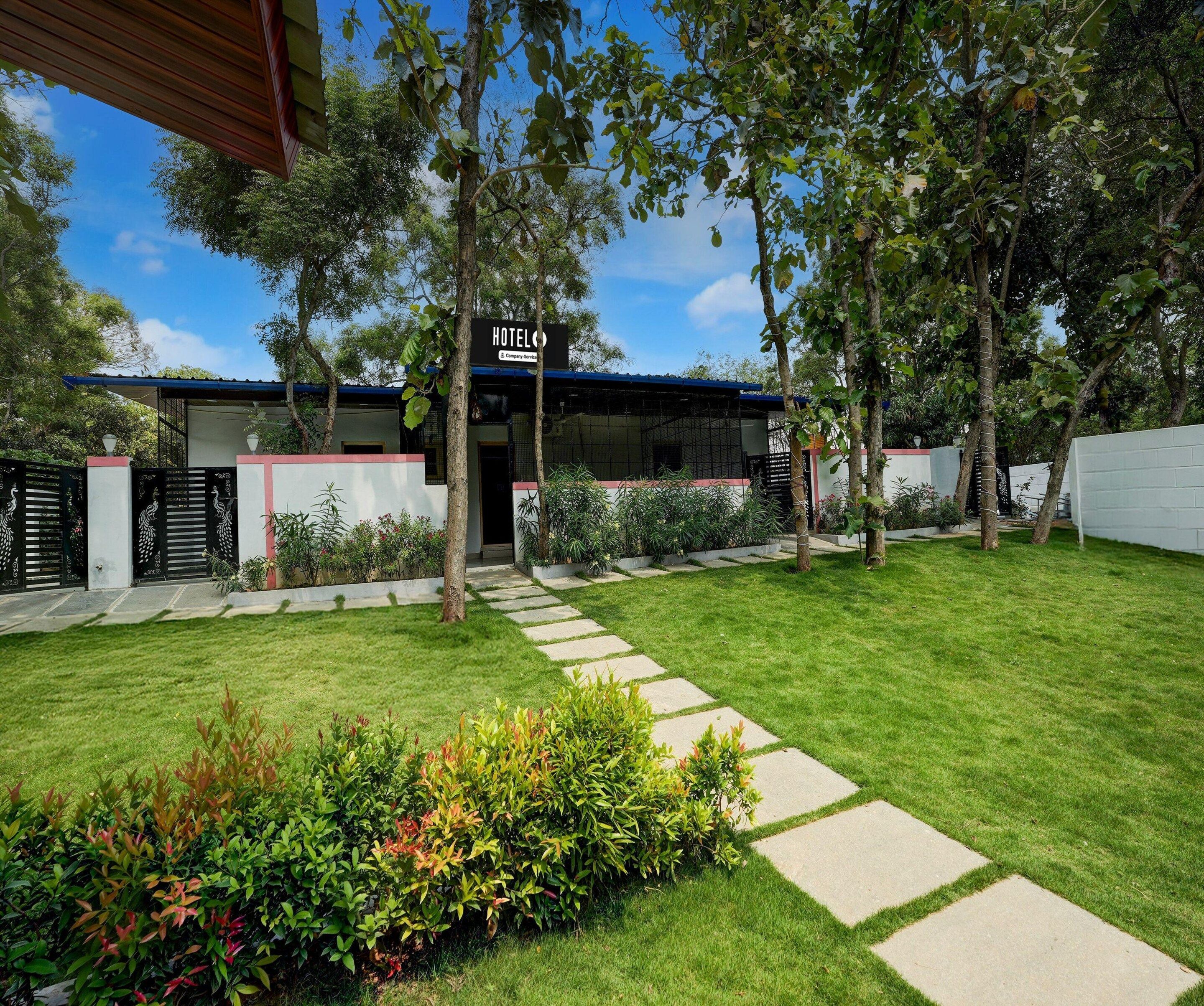 A hotel with a covered entrance, a paved pathway leading to the door, and a well-maintained lawn with various plants.