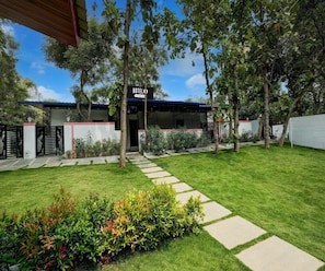 A hotel with a covered entrance, a paved pathway leading to the door, and a well-maintained lawn with various plants. - Classic Kaveri Homestay (Shrirangapattana)
