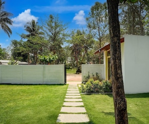 A pathway leading to a building with a white exterior, surrounded by lush greenery and trees. - Classic Kaveri Homestay (Shrirangapattana)