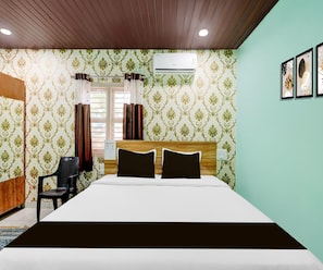 A hotel room with a bed, a desk, and an air conditioning unit. - Classic Kaveri Homestay (Shrirangapattana)