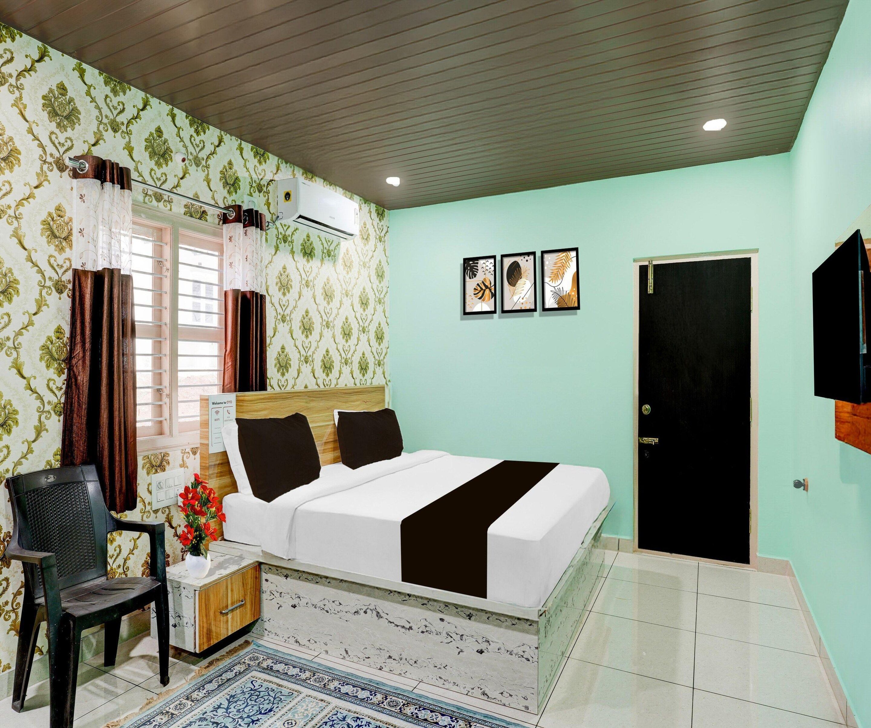 A room with a bed, a chair, a desk with a vase of flowers, a door, and three framed pictures on the wall.
