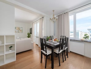 A dining area with a table set for four, surrounded by chairs, a chandelier, and large windows with curtains. - Apartment With Skyline Balcony (Warsaw)