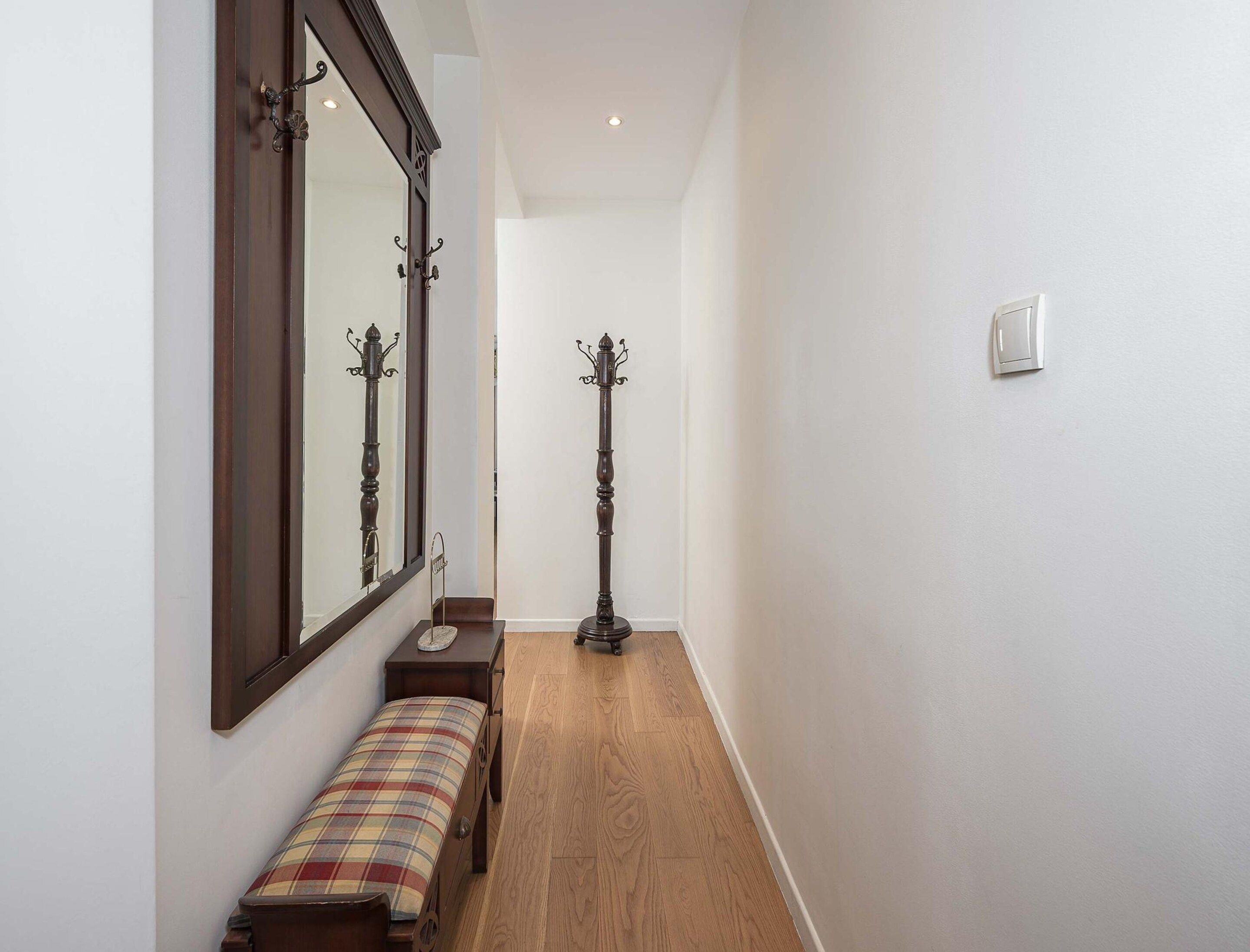 A hallway with a wooden floor, a bench, a coat stand, and a mirror on the wall.