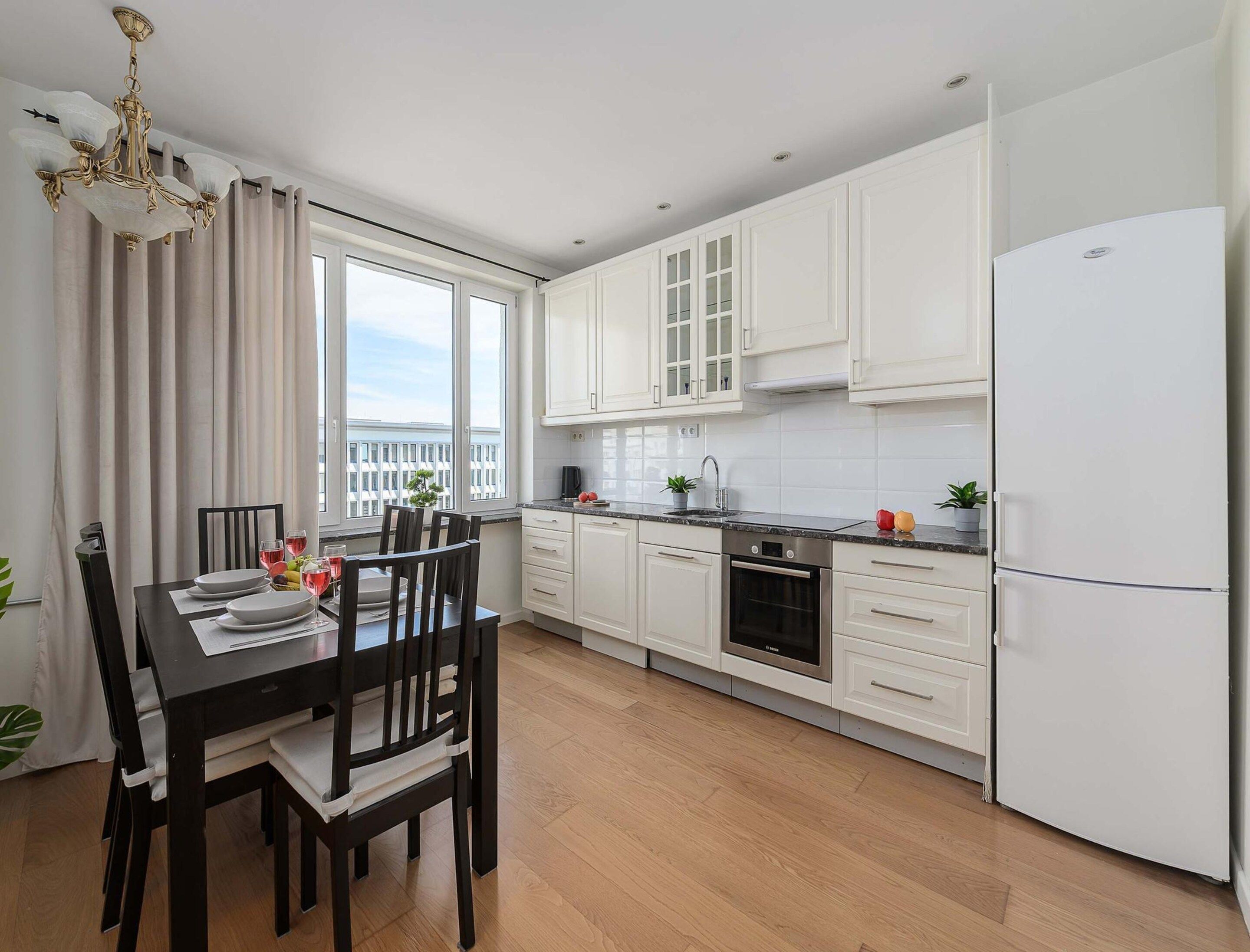 A modern kitchen with white cabinets, a built-in oven, and a stainless steel refrigerator.