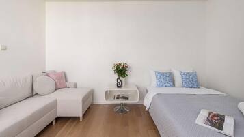 A modern bedroom with a sofa, a bed, a small side table, and a wall-mounted shelf.