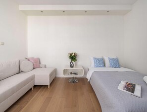A modern bedroom with a sofa, a bed, a small side table, and a wall-mounted shelf. - Apartment With Skyline Balcony (Warsaw)