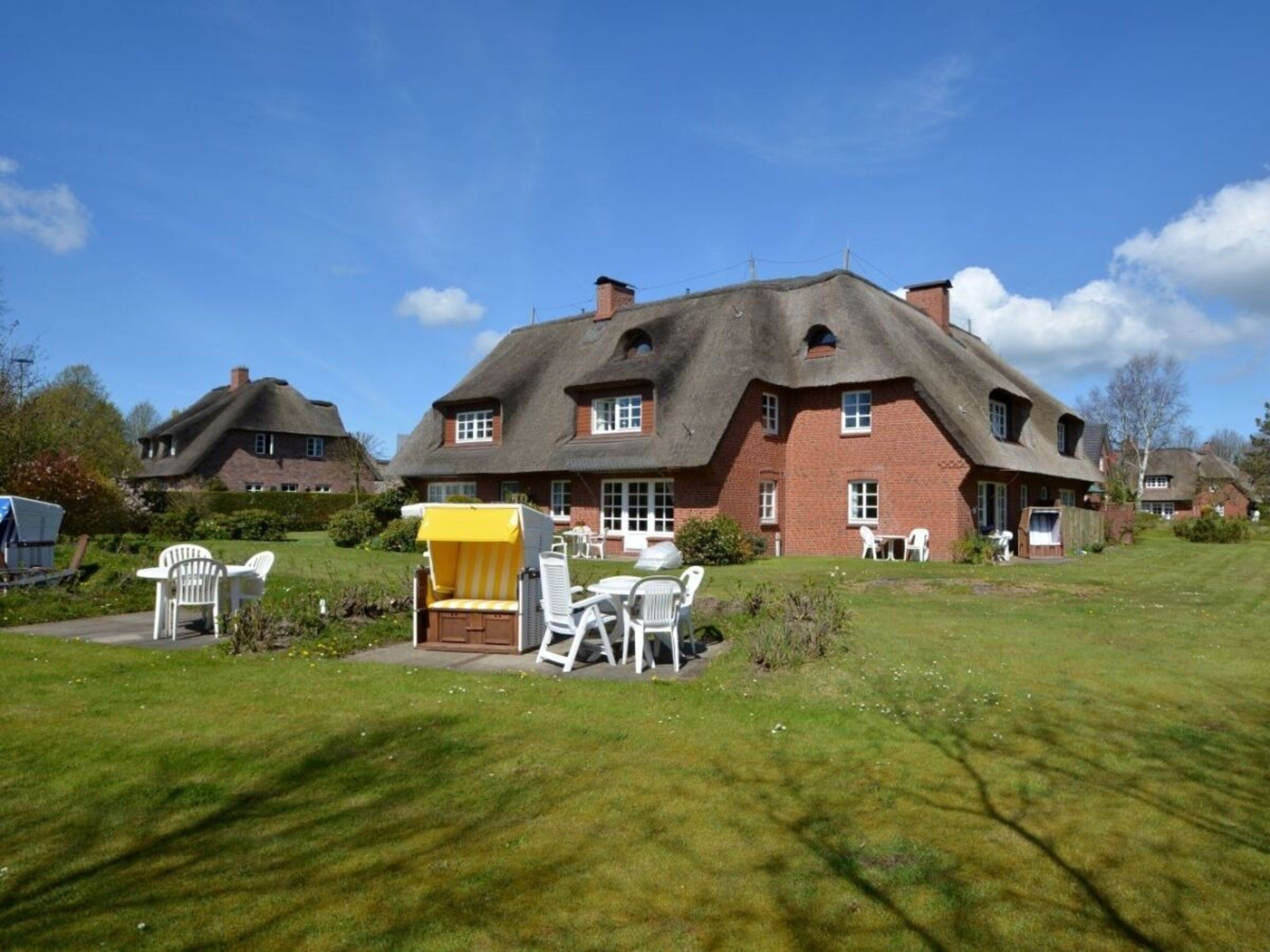A large house with a thatched roof, a patio with outdoor furniture, and a well-maintained lawn.