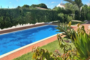 A swimming pool with a brick border, surrounded by well-maintained greenery and a clear sky. - Walking distance to vilamoura marina! apartment with pool and garden (Quarteira)
