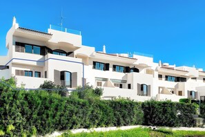 Un immeuble résidentiel moderne à plusieurs étages, doté de balcons, de grandes fenêtres et surplombant un ciel d’un bleu éclatant.