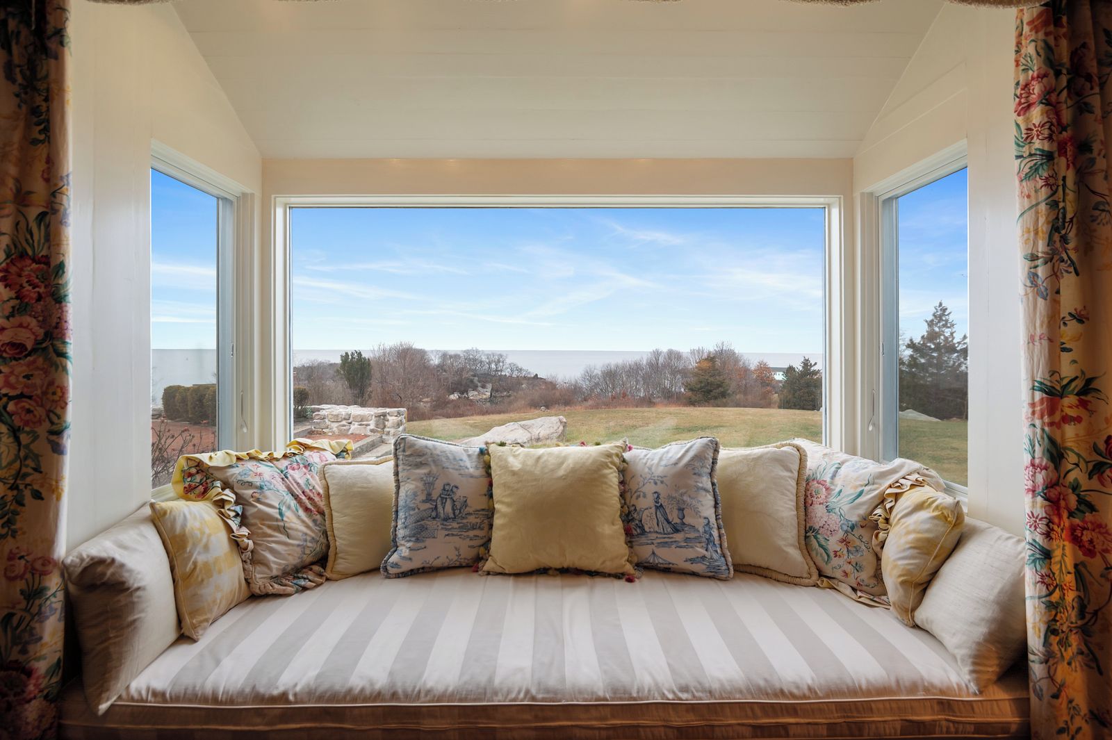 A room with a large window, a cushioned bench, and floral curtains.
