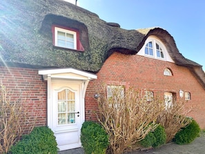 A traditional brick house with a thatched roof, a white door with glass panels, and a small window with a red frame. - Holiday Home in Fohr With 1 Bedroom (Wyk auf Foehr)
