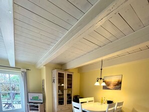 A dining area with a round table, white chairs, a cabinet with glass doors, and a painting on the wall. - Holiday Home in Fohr With 1 Bedroom (Wyk auf Foehr)