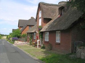 A row of traditional brick houses with thatched roofs, a narrow road, and some greenery. - Holiday Home in Fohr With 1 Bedroom (Wyk auf Foehr)