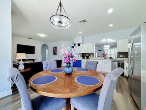 A modern kitchen with white cabinets, a stainless steel refrigerator, and a dining area with a wooden table and blue upholstered chairs. - 6BR Disney Villa, Private Pool/Spa + Resort Access (Kissimmee)