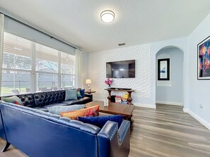 A living room with a sectional sofa, a coffee table, and a flat-screen TV mounted on the wall. - 6BR Disney Villa, Private Pool/Spa + Resort Access (Kissimmee)