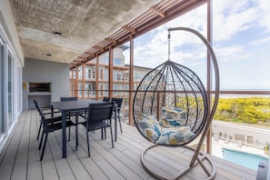 Un balcone con una sedia a dondolo, un tavolo con sedie e vista su un edificio e vegetazione.
