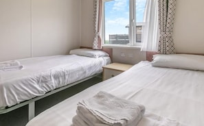 Une chambre d’hôtel avec deux lits simples, une petite table de chevet et une fenêtre avec des rideaux.