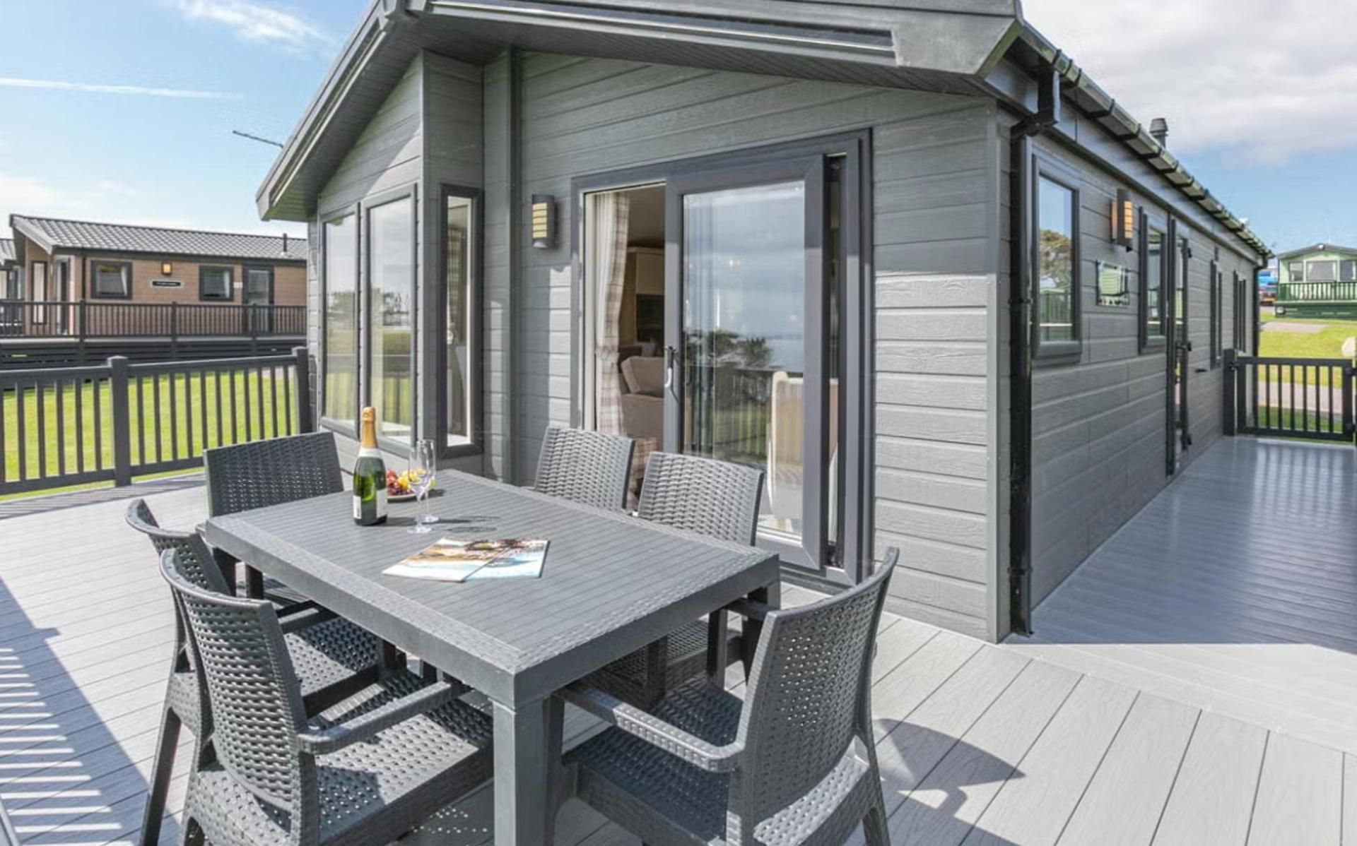 A covered outdoor patio with a table and chairs, a bottle of champagne, and a glass.