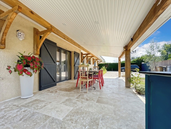 Un patio techado con mesa y sillas, una planta en maceta y vistas al exterior.