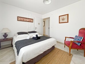 Une chambre d’hôtel avec un lit, une chaise, une lampe et deux tableaux encadrés au mur.