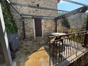 A stone building with a wooden door, a covered outdoor seating area with metal chairs, and a grill. - Cottage 'Joannet' with Mountain View, Private Terrace and Wi-Fi (Lamastre)