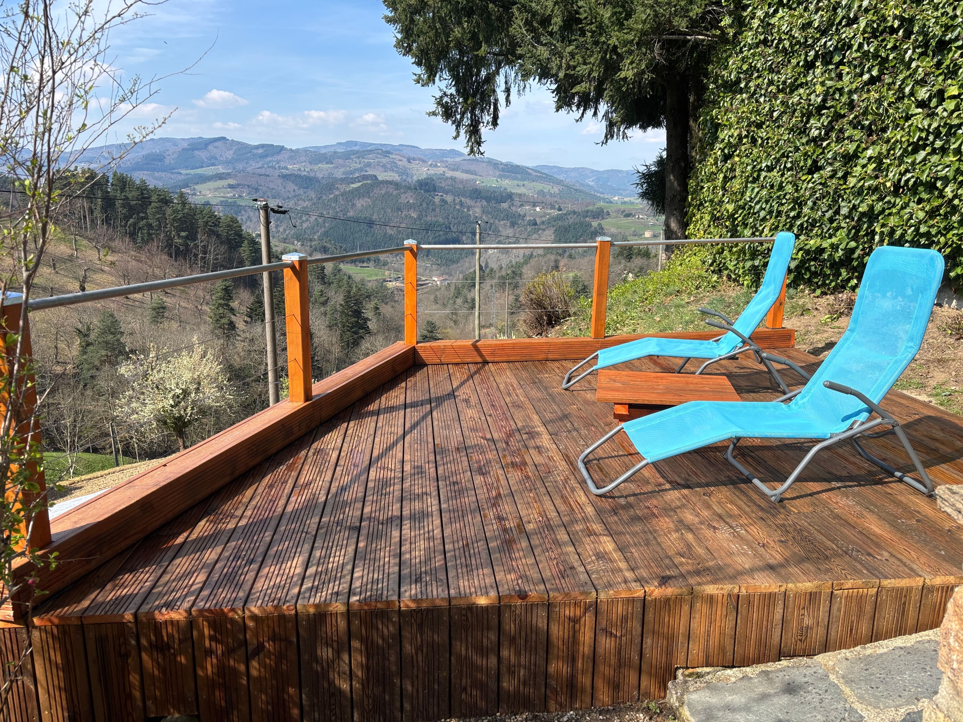 A wooden deck with two blue lounge chairs, overlooking a mountainous landscape.