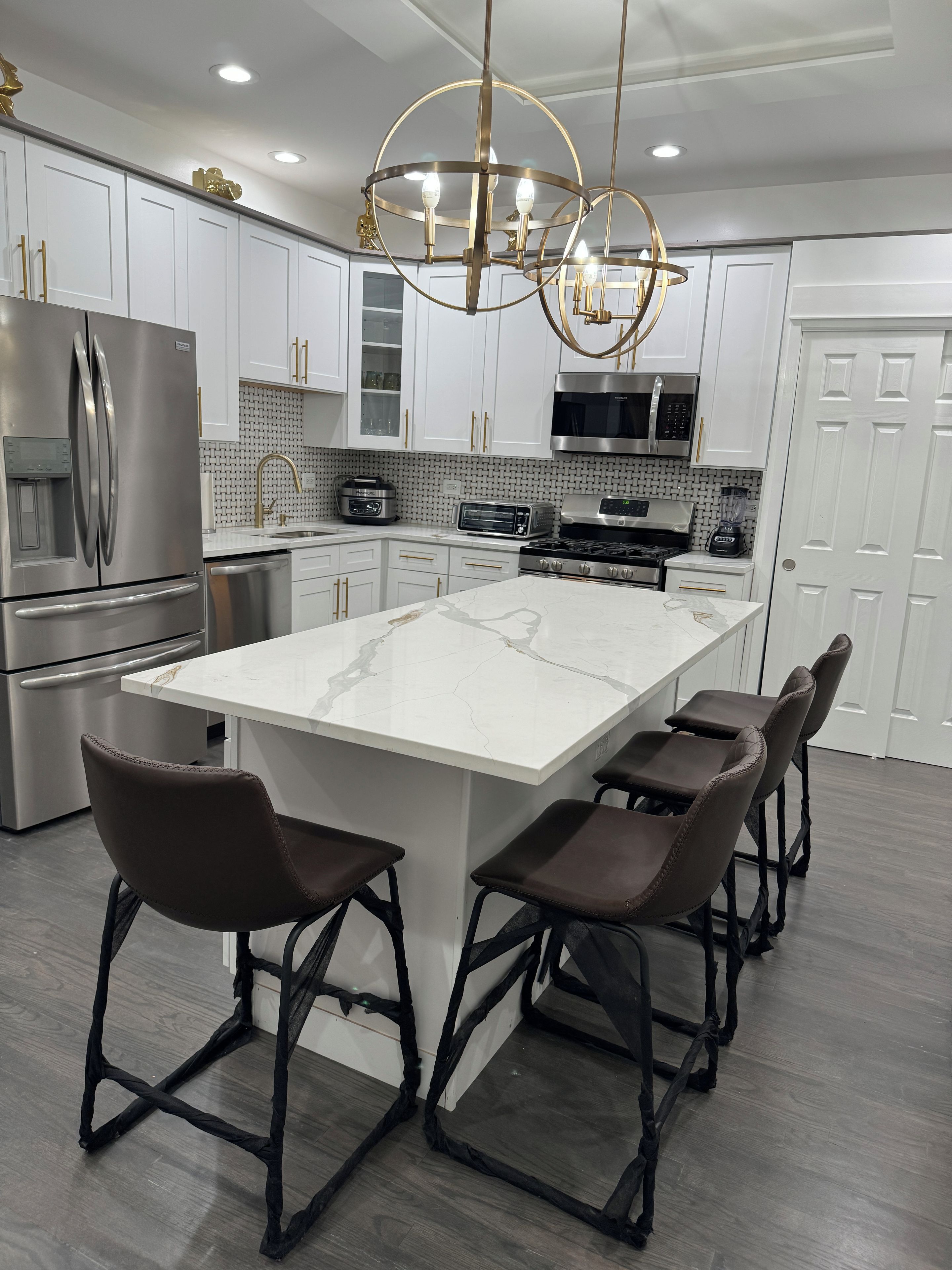 A modern kitchen with a large island, stainless steel appliances, and a chandelier.