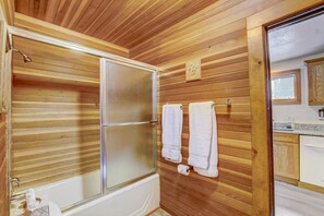 Een betegelde badkamer met een glazen douchecabine, witte handdoeken en een toiletrol.