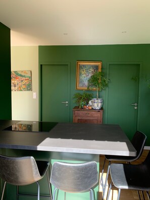 A dining area with a table, chairs, a cabinet with plants, and artwork on the wall.