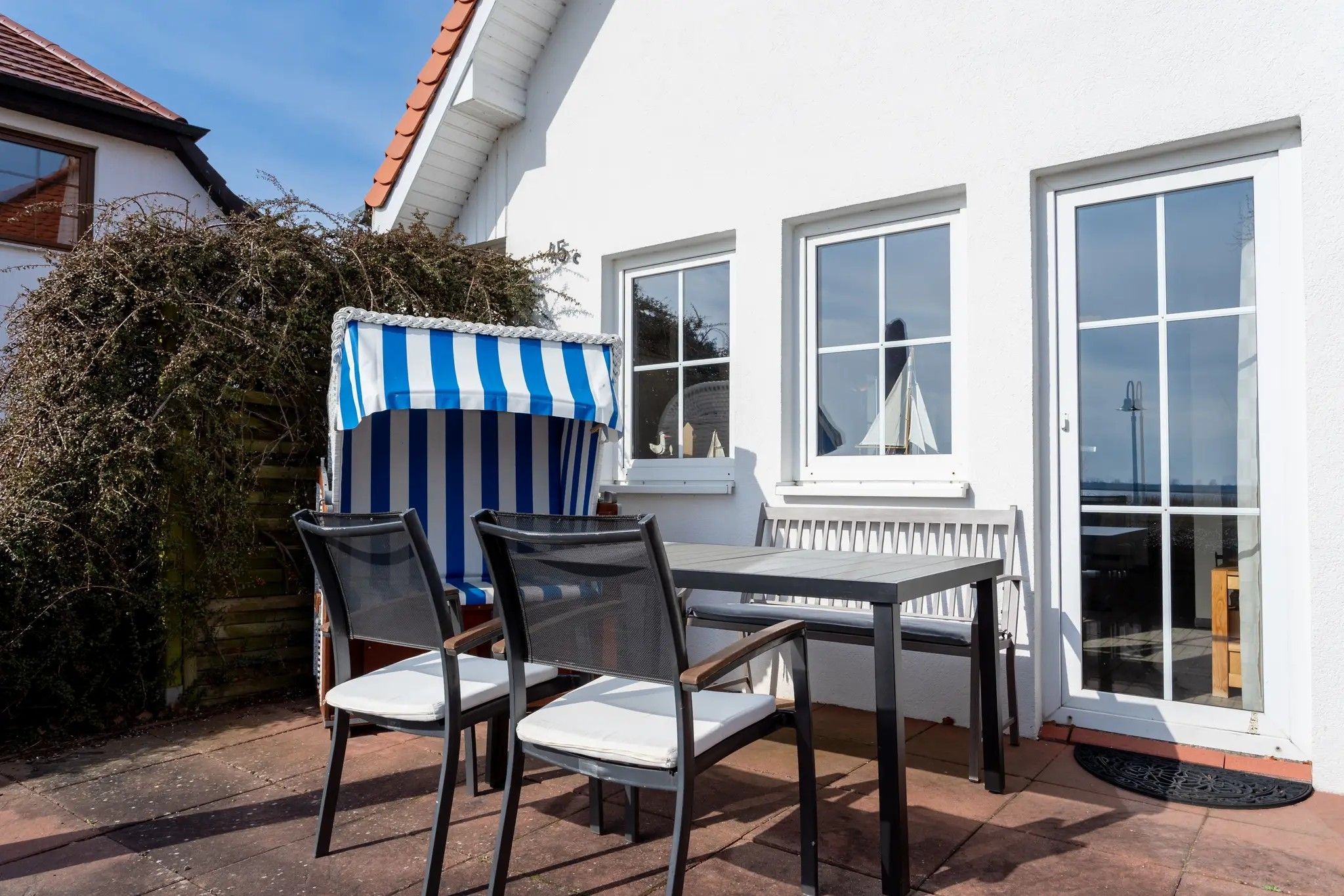 Eine Terrasse im Freien mit Tisch und Stühlen, einem Streifen-Jalousie und einem weißen Gebäude mit Fenstern.