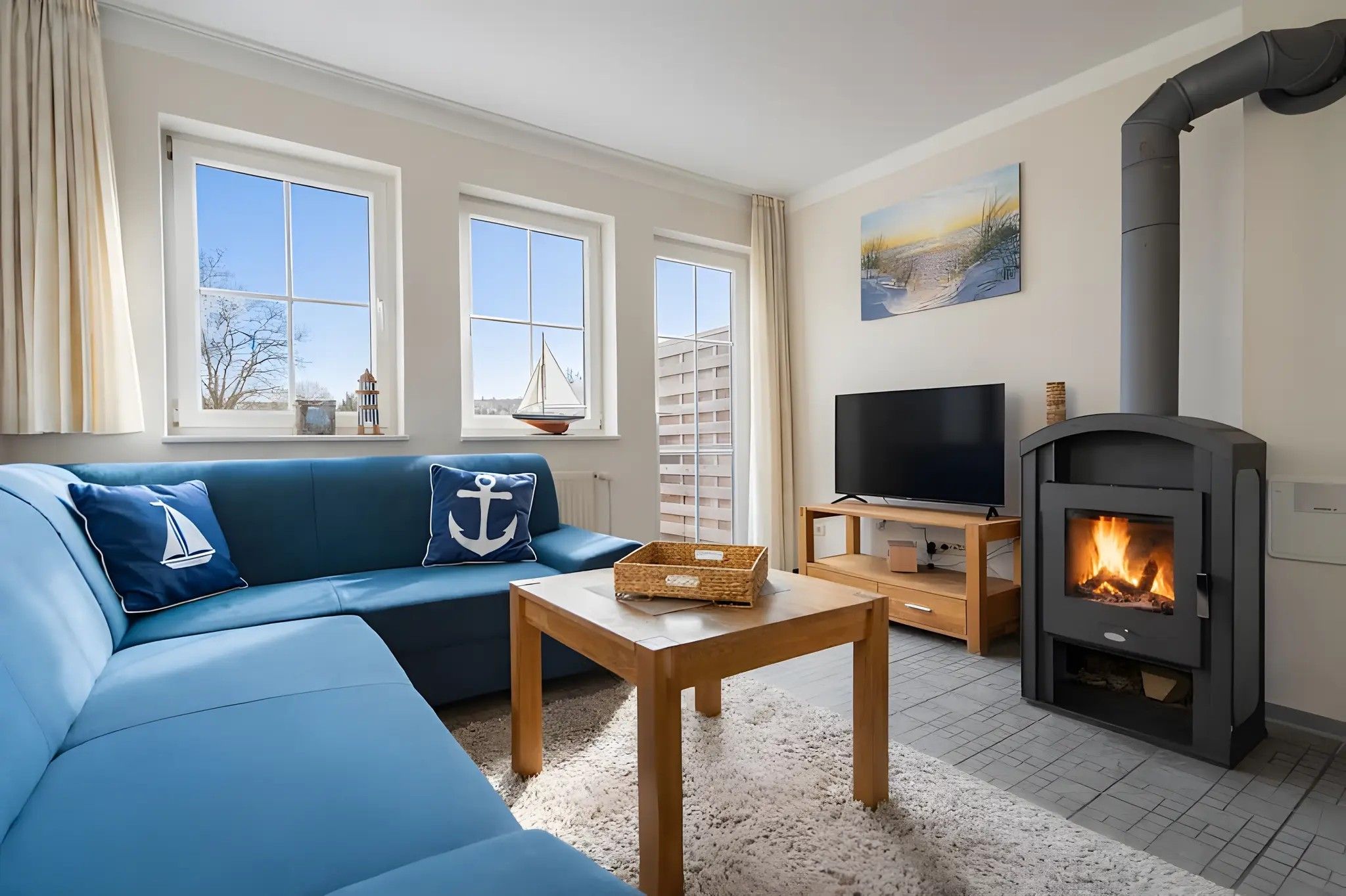 A living room with a blue sofa, a television, a fireplace, and windows with a view of the outside.