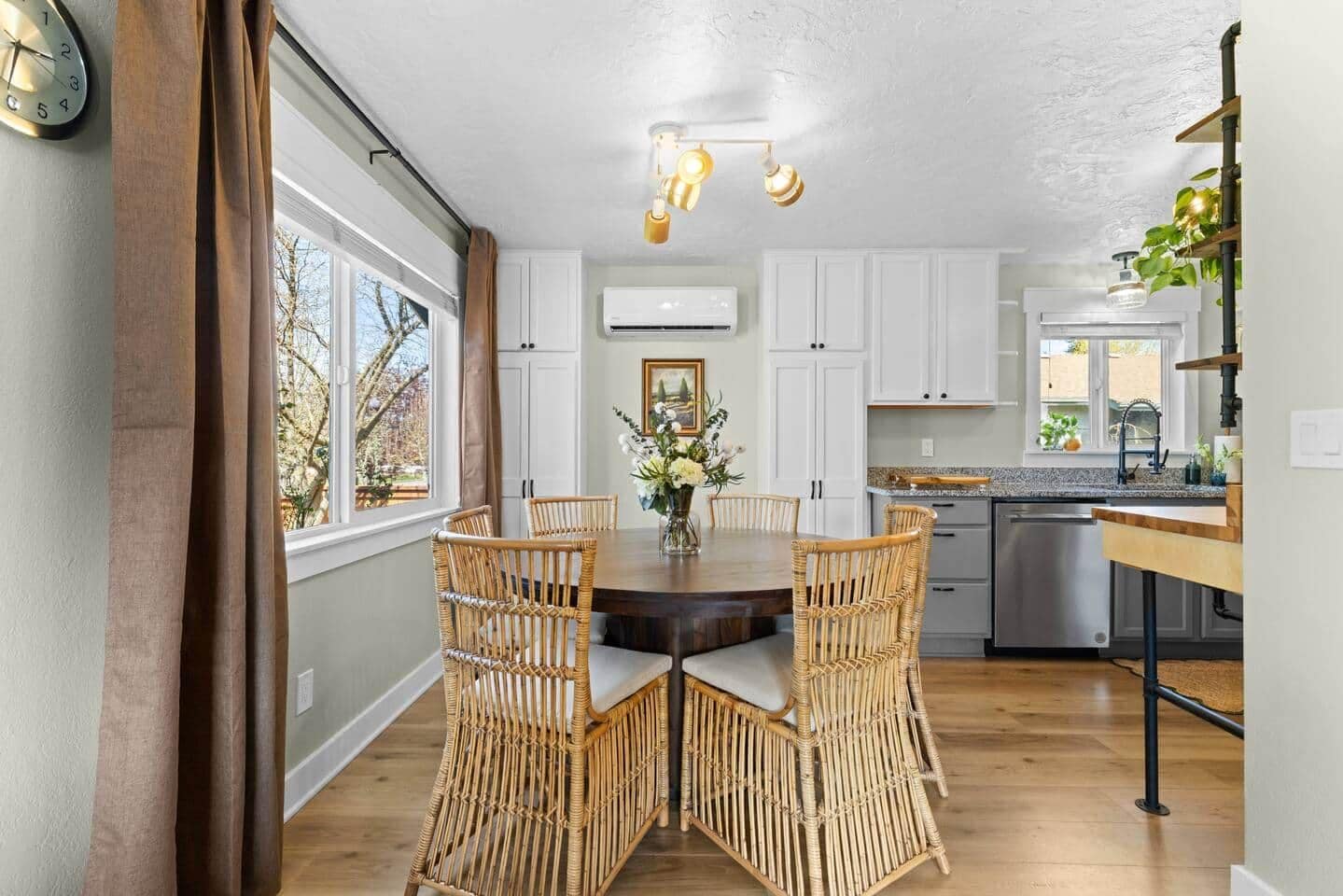 A dining area with a round table, wicker chairs, and a vase with flowers.