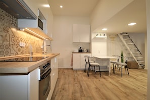 A compact kitchen with a wooden countertop, built-in oven, and a dining area with a white table and chairs. - Roxy Stúdió 4A - Budapest (Budapest)