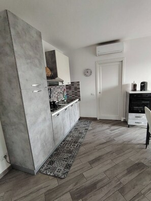 A modern kitchen with a grey cabinet, a stove, and a sink. There is a patterned rug on the floor and a white door in the background. - New Listing (Porto Torres)