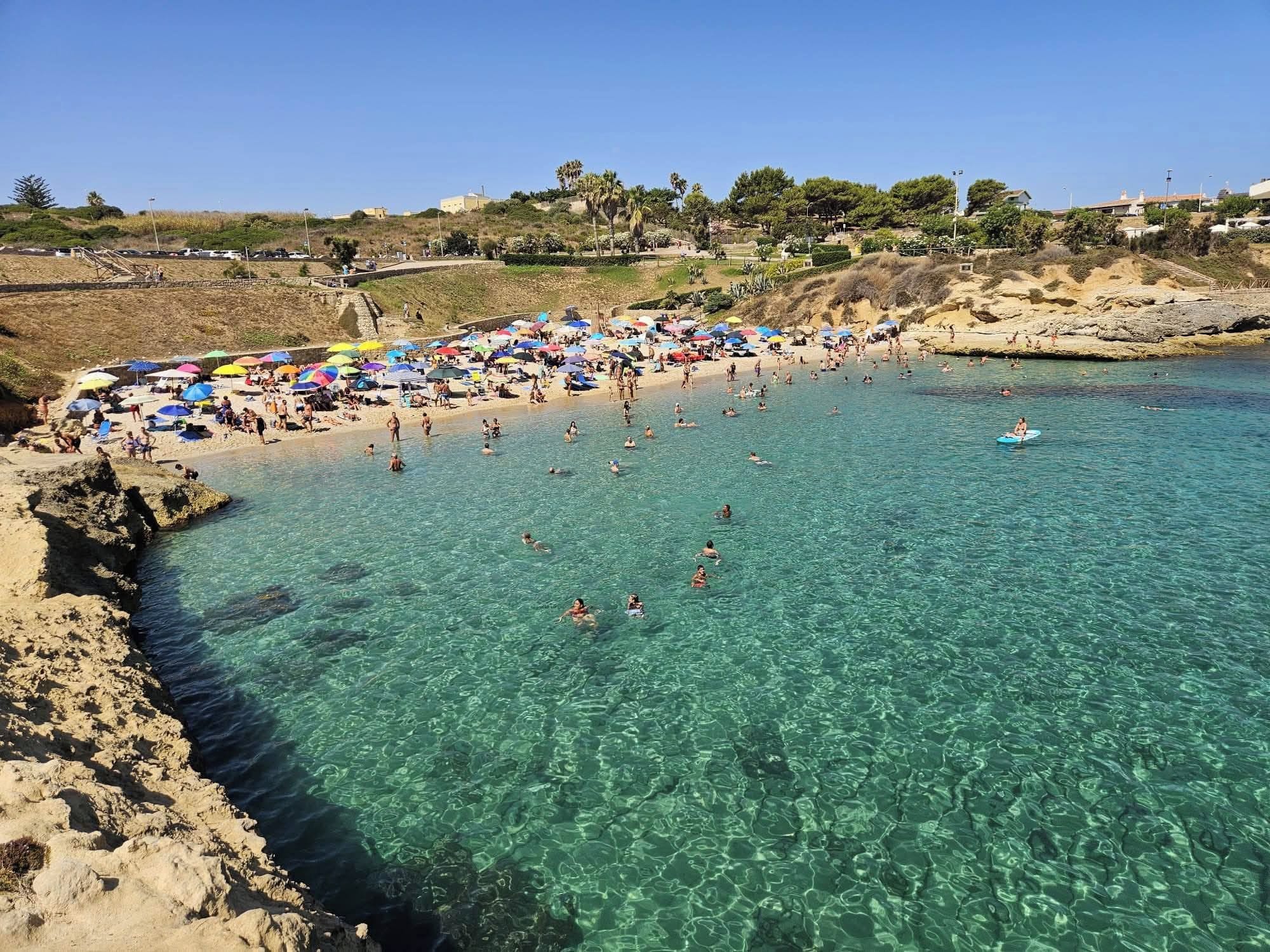A beach with clear water, umbrellas, and people swimming.