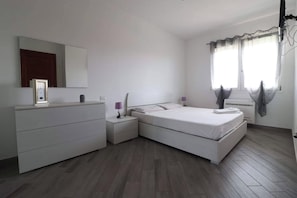 A bedroom with a bed, a dresser, a nightstand, a mirror, and a window with curtains. - New Listing (Porto Torres)