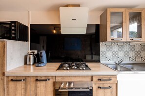 A modern kitchen with a gas stove, a kettle, and a coffee maker. - Ar Penty a Flore - Piscine - Sauna (Saint-Jean-la-Poterie)