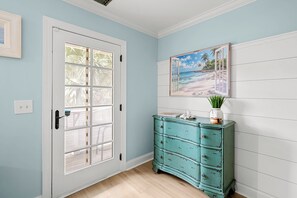 A hallway with a white door, a teal dresser, and a beach-themed picture on the wall. - Old Town Bluffton Condo Near May River (Bluffton)