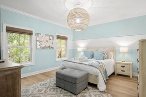A bedroom with a bed, bedside tables, a bench, and a chandelier. - Old Town Bluffton Condo Near May River (Bluffton)