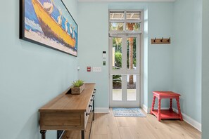 A room with a wooden desk, a red stool, a door with glass panels, and a painting on the wall. - Old Town Bluffton Condo Near May River (Bluffton)