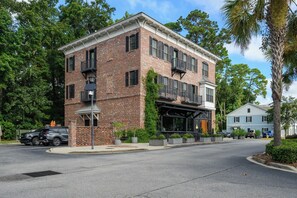 A multi-story brick building with a covered outdoor seating area and a visible entrance. - Old Town Bluffton Condo Near May River (Bluffton)