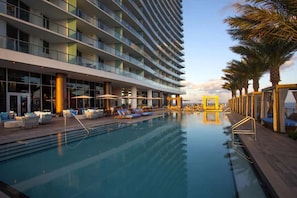 Un hotel amb piscina, mobiliari exterior i palmeres.
